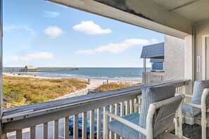 A balcony with a view of the beach and ocean, featuring a wooden railing and striped chairs.