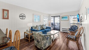 A living room with a blue sofa, wooden chairs, a coffee table, and a dining table. - A Place at the Beach V A204, Ocean View Comfort Awaits You in Myrtle Beach (Myrtle Beach)