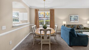 A dining area with a round table, six chairs, a chandelier, and a window with curtains.