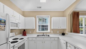 A kitchen with white cabinets, a microwave, a stove, and a sink.