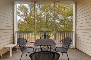 A covered patio with a table and chairs, a bench, and a view of trees through a railing. - Arbor Trace 322, Condo by the Greens, Relaxing Golf Views Await (North Myrtle Beach)
