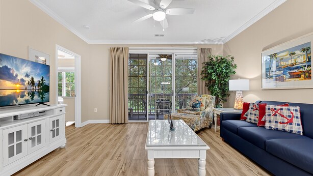 A living room with a TV, white cabinet, glass coffee table, blue sofa, and a ceiling fan. - Arbor Trace 322, Condo by the Greens, Relaxing Golf Views Await (North Myrtle Beach)