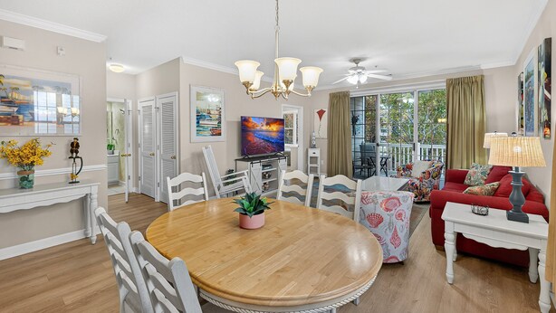 A spacious living room with a wooden dining table, white chairs, a red sofa, and a television. - Arbor Trace 724, Tranquil Golf Views, Walk to Tee Time Daily (North Myrtle Beach)