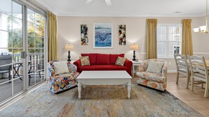 A living room with a red sofa, two patterned armchairs, a white coffee table, and a large window with curtains. - Arbor Trace 724, Tranquil Golf Views, Walk to Tee Time Daily (North Myrtle Beach)