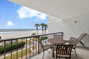 Un balcon avec vue sur la plage, une table avec des chaises et un mur décoré de motifs.
