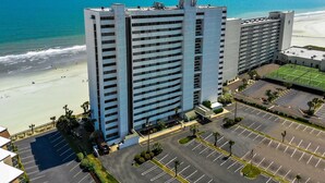 A high-rise hotel with multiple floors, a parking lot, and a beach view.
