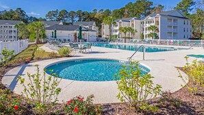 A hotel with a circular pool surrounded by lounge chairs and umbrellas, with buildings in the background. - River Oaks Getaway | Golf, Beach, Fun – All in One! | Fairways 26E (Myrtle Beach)