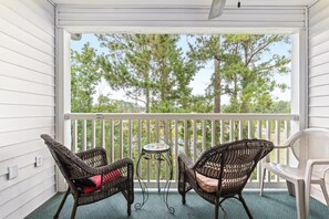 A covered porch with two wicker chairs, a small table, and a view of trees.
