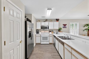 A modern kitchen with white cabinets, stainless steel appliances, and a wooden floor.