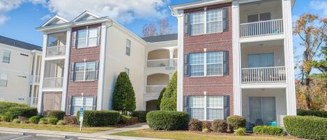 A multi-story apartment building with balconies, a parking lot, and well-maintained landscaping.