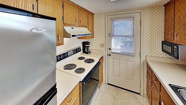 A compact kitchen with a refrigerator, stove, microwave, and wooden cabinets. - Beach Cottage Retreat | Relax by the Shore & Golf | GC 6 (Myrtle Beach)