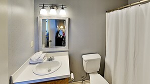 A bathroom with a white sink, a mirror with lights, a toilet, and a shower curtain. - Beach Cottage Retreat | Relax by the Shore & Golf | GC 6 (Myrtle Beach)