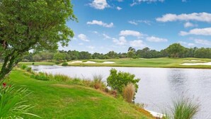 A golf course with a pond, trees, and a clear sky.