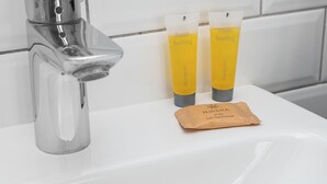 Un lavamanos con grifo de cromo, dos botellas amarillas de champú y una pastilla de jabón marrón.