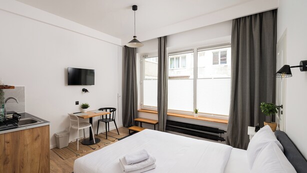 Una habitación de hotel moderna con una cama, escritorio, silla y televisor montado en la pared.