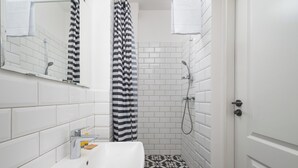Un baño con un lavabo blanco, una ducha con cortina a rayas y suelo de baldosas.