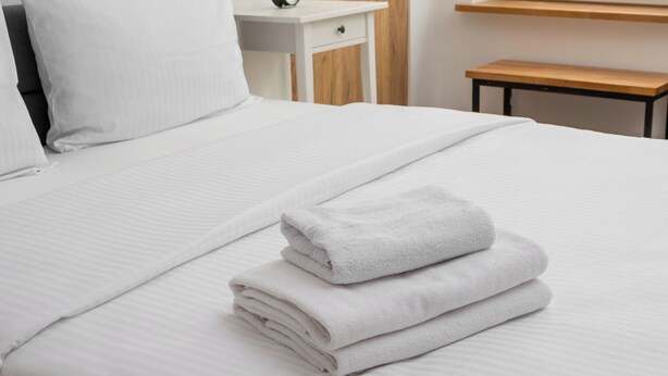 Un lit bien fait, avec des draps blancs et une serviette pliée posée sur le dessus.