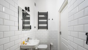 Une petite salle de bain avec des carreaux de céramique blancs rectangulaires, un lavabo blanc, des toilettes et un porte-serviettes.