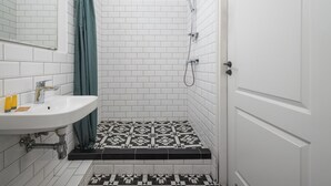 Een badkamer met een wit wastafelmeubel, een spiegel, een douche met een groen gordijn en een betegelde vloer.