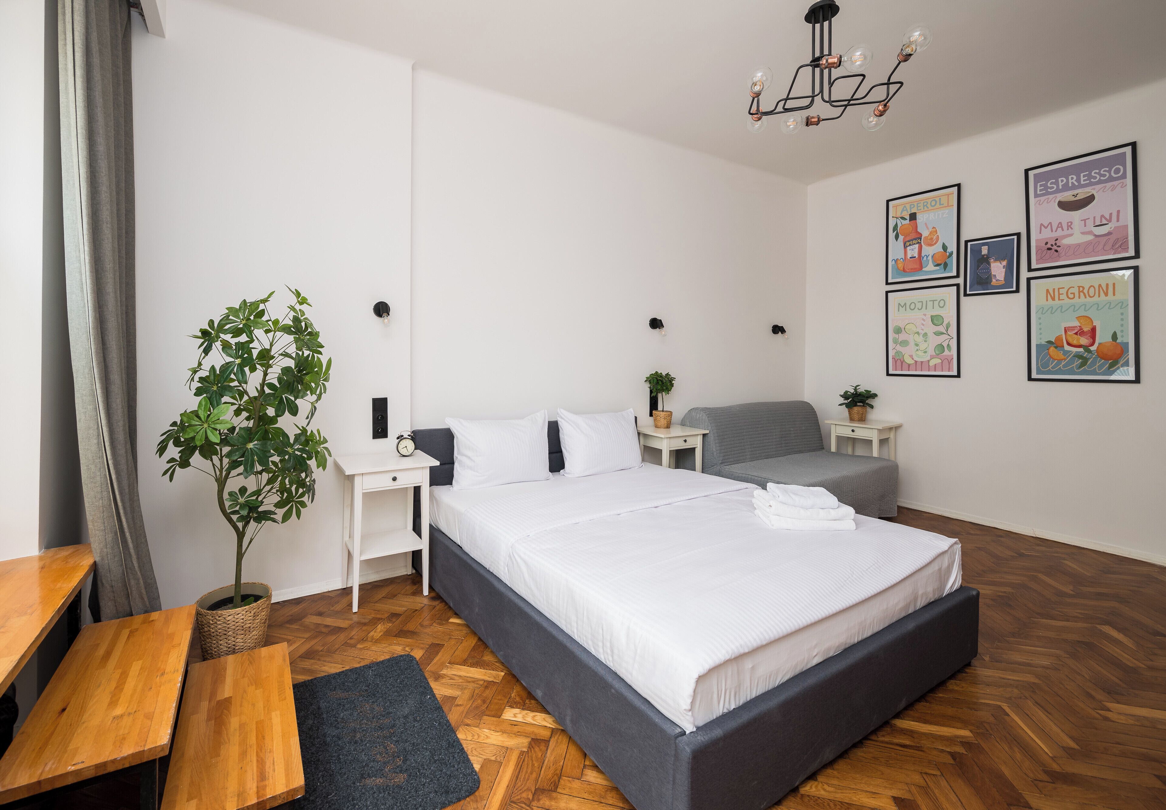 Ein modernes Schlafzimmer mit einem großen Bett, Nachttischen, einem Schreibtisch und einer Topfpflanze.