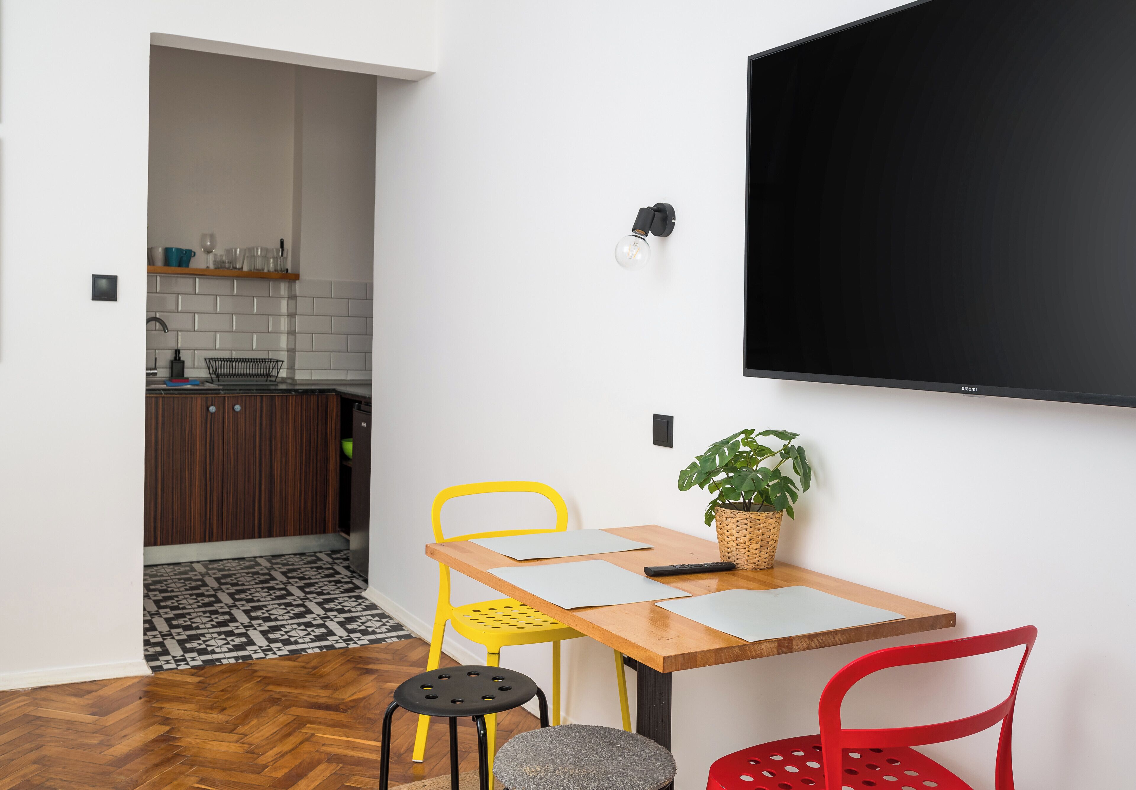 A dining area with a wooden table, two chairs, a potted plant, and a wall-mounted TV.