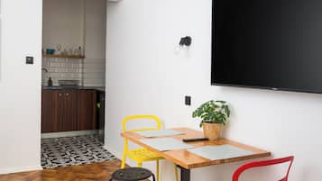 A dining area with a wooden table, two chairs, a potted plant, and a wall-mounted TV.