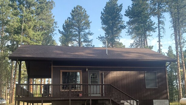 A cabin with a wooden exterior, a covered porch, and a staircase leading to the main entrance.