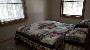 A bedroom with a bed, two windows, and a carpeted floor.