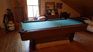 A pool table in a room with wooden flooring, a window, and a small television.
