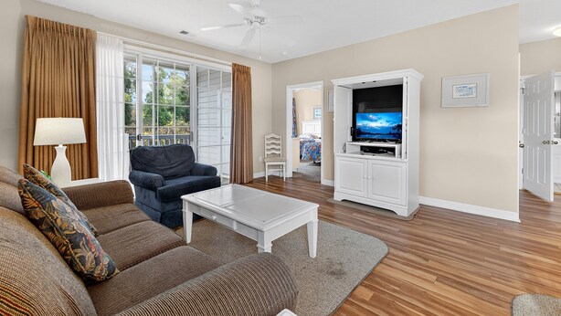 A living room with a sofa, a coffee table, a TV, and a ceiling fan. - North Myrtle Beach | Your Golf & Beach Getaway | IW721 (North Myrtle Beach)