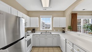 A kitchen with white cabinets, a stainless steel refrigerator, a microwave, and a sink. - North Myrtle Beach | Your Golf & Beach Getaway | IW721 (North Myrtle Beach)