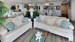 A modern living room with a sectional sofa, a glass coffee table, and a dining area in the background. - Kingston Plantation South Hampton (Myrtle Beach)