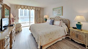 A spacious bedroom with a large bed, a desk with a computer, and a view of the city through the window. - Kingston Plantation South Hampton (Myrtle Beach)