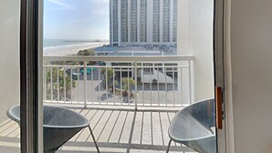 A balcony with two chairs, a view of a beach, and a tall building in the background. - Kingston Plantation South Hampton (Myrtle Beach)