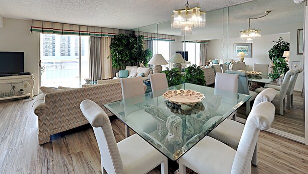 A spacious living room with a glass dining table, modern furniture, and a large window offering a city view. - Kingston Plantation South Hampton (Myrtle Beach)