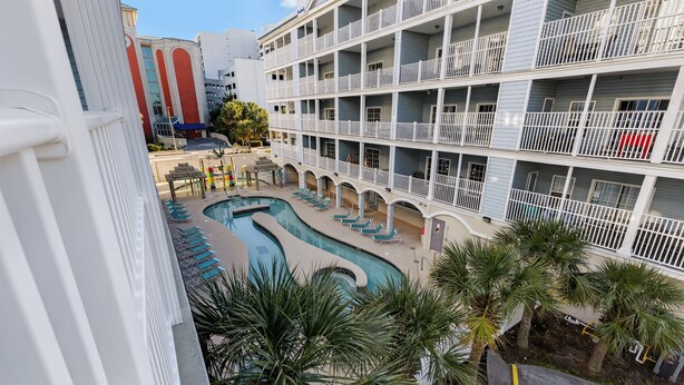 Un hôtel à plusieurs étages doté d’une piscine, de balcons et de palmiers.