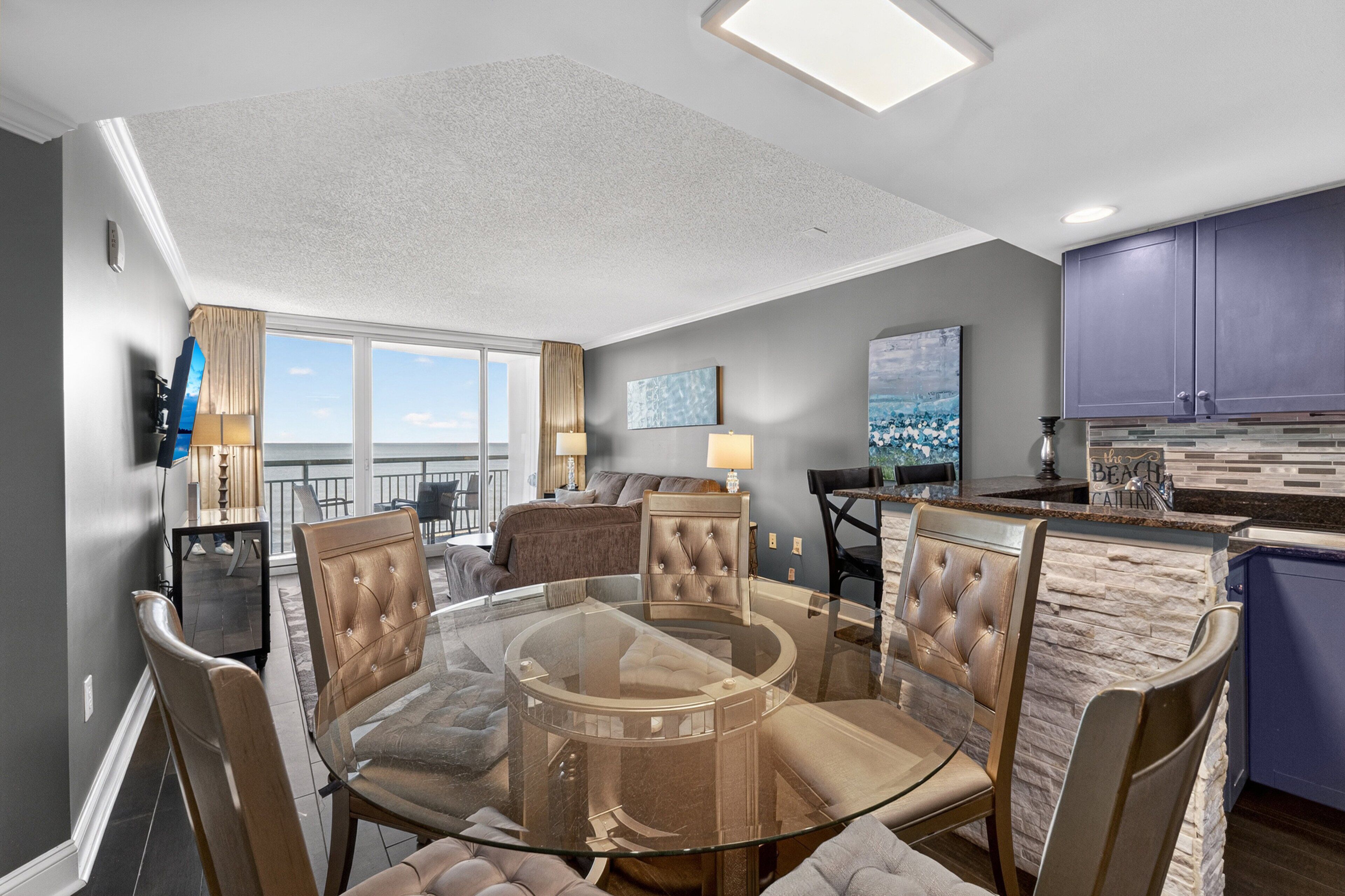 A modern living room with a glass coffee table, leather chairs, a sofa, and a view of the ocean.