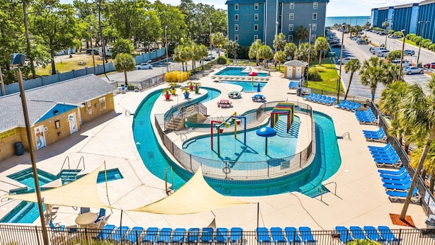 A pool area with multiple swimming pools, lounge chairs, and a building in the background.