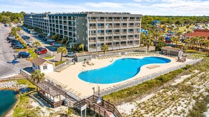 A hotel with a large pool, a parking lot, and a beach area.