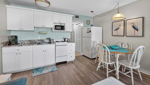 Une cuisine avec des meubles blancs, un four à micro-ondes, une cuisinière et un coin repas comprenant une table et des chaises.
