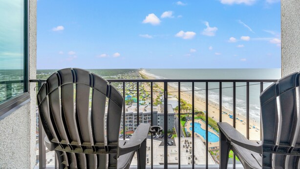 A balcony with two chairs, a pool, and a beach view.