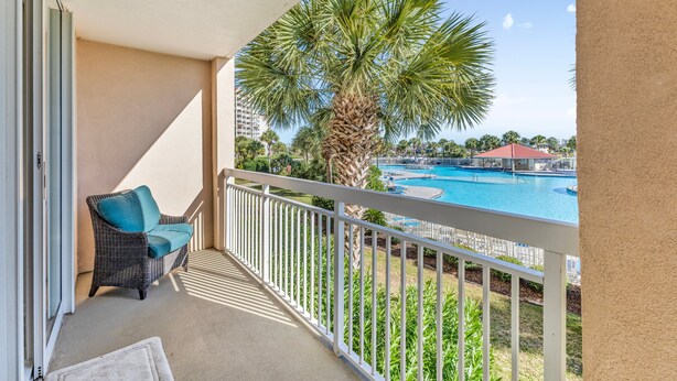 Een balkon met een rieten stoel en uitzicht op een zwembad en palmbomen.