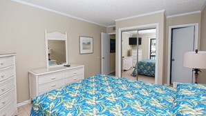 A bedroom with a large bed, a dresser, a mirror, and a door leading to another room. - Pelican Landing 125 - Myrtle Beach (Myrtle Beach)