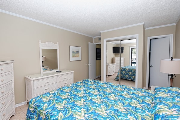 Une chambre à coucher avec un grand lit, une commode, un miroir et une porte donnant sur une autre pièce.