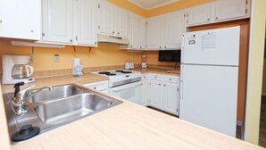 A kitchen with white cabinets, a stainless steel sink, a stove, and a refrigerator. - Pelican Landing 125 - Myrtle Beach (Myrtle Beach)