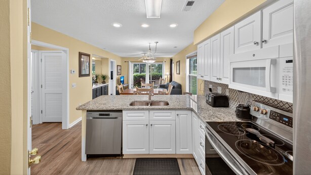 A modern kitchen with white cabinets, a stainless steel dishwasher, a double sink, a microwave, and a gas stove. - Myrtle Beach Fun | Golf & River Oaks Awaits You! | RO 5C (Myrtle Beach)