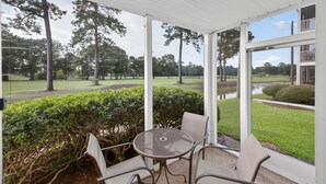 A covered patio with a round metal table and four chairs, overlooking a well-maintained lawn and trees. - Myrtle Beach Fun | Golf & River Oaks Awaits You! | RO 5C (Myrtle Beach)
