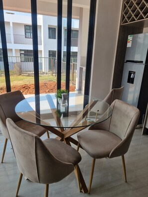 Contemporary space with a glass-top table and two chairs, offering a view of a building with balconies and a fenced outdoor area.