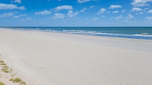 A wide sandy beach with a clear blue sky and a distant pier.
