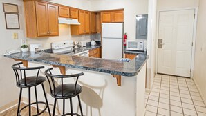 A kitchen with wooden cabinets, a granite countertop, a stove, a microwave, and two bar stools.